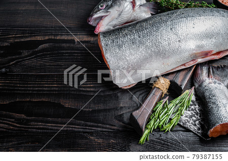 Raw cut salmon fish on a wooden cutting board with chef cleaver. Black Wooden background. Top view. Copy space Raw cut salmon fish on a wooden cutting board with chef cleaver. Black Wooden background. Top view. Copy space 79387155