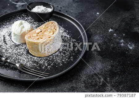 Apple strudel with cinnamon, powdered sugar and vanilla ice cream on a plate. Black background. Top view. Copy space 79387187