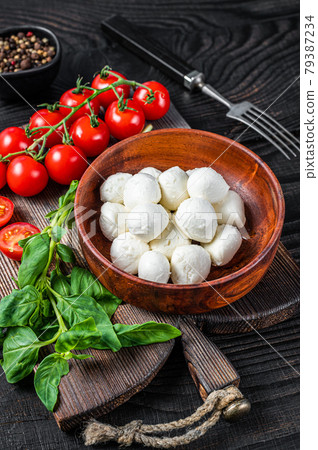 Italian mini Mozzarella cheese balls, basil and tomato cherry ready for cooking Caprese salad. Black wooden background. Top view 79387234