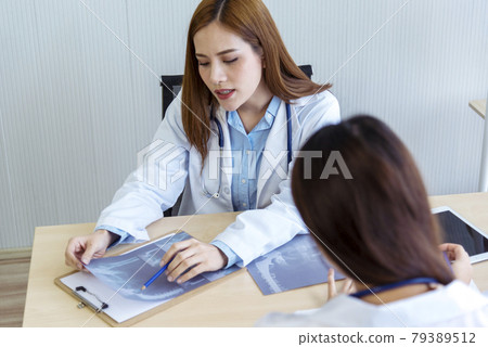 Two asian women doctors discuss meeting doctor's office medical clinic looking x-ray film consulting patient disease. Asian medical lab young women talking together discussing healthcare teamwork Two asian women doctors discuss meeting doctor's office medical clinic looking x-ray film consulting patient disease. Asian medical lab young women talking together discussing healthcare teamwork 79389512