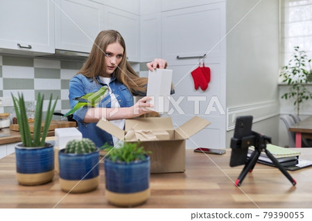 Woman recording video on smartphone unpacking cardboard box. Pet parrot helping to unpack Woman recording video on smartphone unpacking cardboard box. Pet parrot helping to unpack 79390055
