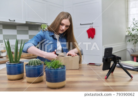 Woman recording video on smartphone unpacking cardboard box. Pet parrot helping to unpack Woman recording video on smartphone unpacking cardboard box. Pet parrot helping to unpack 79390062