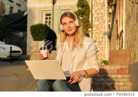 Young beautiful female in headphones with laptop drinking coffee in paper cup Young beautiful female in headphones with laptop drinking coffee in paper cup 79390333