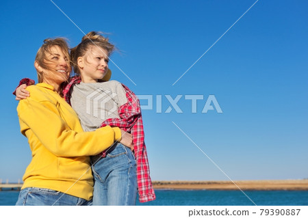 Outdoor portrait of happy mom and child daughter hugging together, blue sky background Outdoor portrait of happy mom and child daughter hugging together, blue sky background 79390887