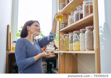Organization of pantry, woman in kitchen near wooden rack with cans and containers of food 79390929