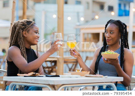 Latina women doing a toast while eating takeaway food outdoors Latina women doing a toast while eating takeaway food outdoors 79395454