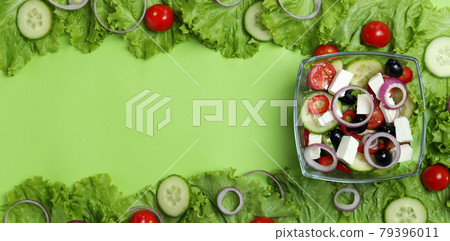 Bowl of greek salad and ingredients on green background, space for text 79396011