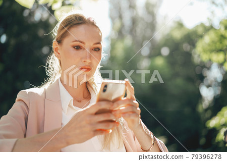 Successful young businesswoman sitting in outdoor cafe and using smartphone Successful young businesswoman sitting in outdoor cafe and using smartphone 79396278