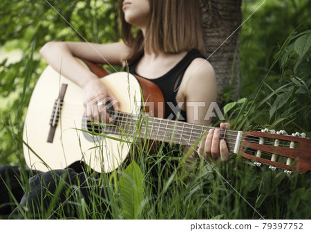 Teenager girl playing guitar in park Teenager girl playing guitar in park 79397752