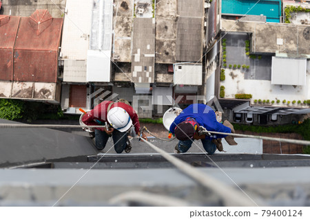 Asian painters hanging on rope painting color on building wall. Asian painters hanging on rope painting color on building wall. 79400124