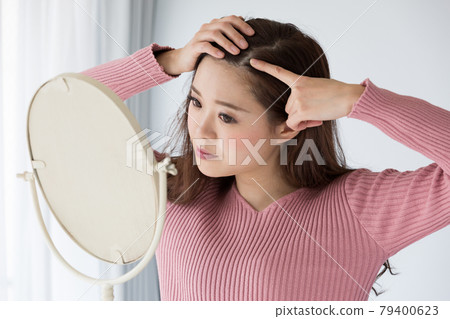 Woman looking at scalp with mirror Woman looking at scalp with mirror 79400623