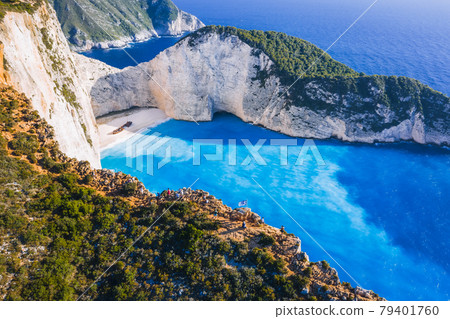 Aerial view of Navagio Beach - Shipwreck beach - on Zakynthos Island, Greece. Tourists on cliff edge enjoy view on summer travel trip 79401760