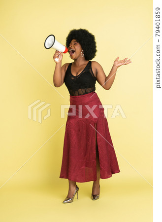 Portrait of African young woman shouting at megaphone isolated over light yellow studio background. Concept of human emotions, facial expression, youth, sales, ad. Portrait of African young woman shouting at megaphone isolated over light yellow studio background. Concept of human emotions, facial expression, youth, sales, ad. 79401859