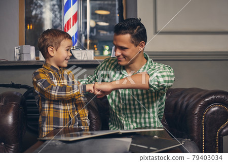 Young father and his stylish little son in the barbershop in the waiting room. 79403034