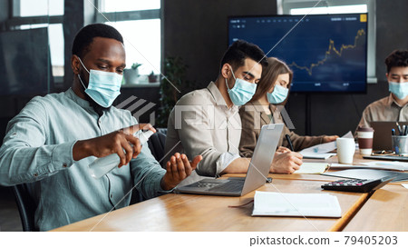 Multicultural workers wearing medical masks, black man using antibacterial sanitizer 79405203