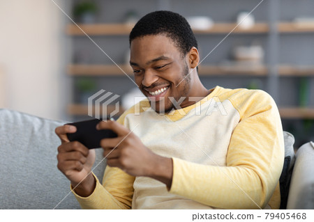 Happy black guy playing game on mobile phone Happy black guy playing game on mobile phone 79405468