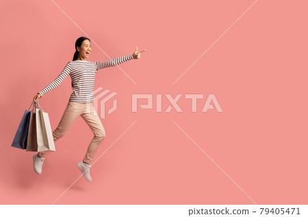 Shocking Sales. Excited Asian Woman Jumping With Shopping Bags And Pointing Aside Shocking Sales. Excited Asian Woman Jumping With Shopping Bags And Pointing Aside 79405471