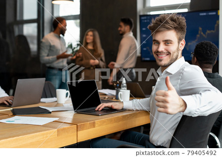 Confident businessman sitting at desk showing thumbs up gesture Confident businessman sitting at desk showing thumbs up gesture 79405492