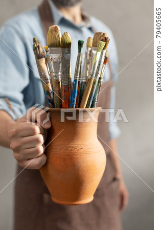 Man artist painter holding clay jug with paint brush. Painter artist and paintbrush in studio 79405665