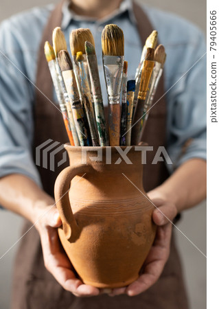 Man artist painter holding clay jug with paint brush. Painter artist and paintbrush in studio 79405666