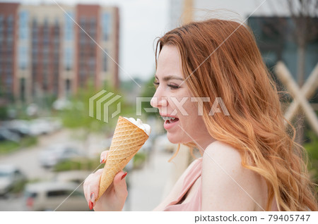 Portrait of young beautiful red-haired woman smiling with braces and going to eat ice cream cone outdoors in summer 79405747