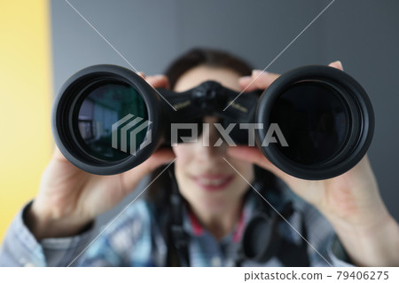 Young woman looking through black professional binoculars closeup 79406275