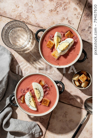 Two bowls Spanish salmorejo soup with spoon, napkin and croutons on a textured background pink tiles top view Two bowls Spanish salmorejo soup with spoon, napkin and croutons on a textured background pink tiles top view 79407650
