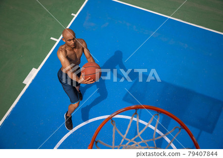 High angle view of young man, male basketball player playing basketball at street public stadium, sport court or palyground outdoors. Summer sport games. High angle view of young man, male basketball player playing basketball at street public stadium, sport court or palyground outdoors. Summer sport games. 79407844