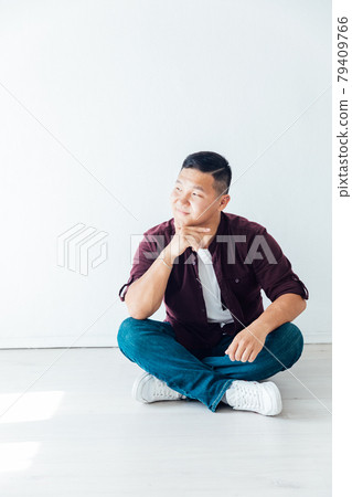 Beautiful Asian man sits on the floor in a white room 79409766