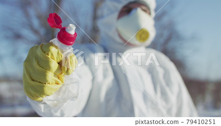 Man in protective costume and glove constricts plastic bottle Man in protective costume and glove constricts plastic bottle 79410251
