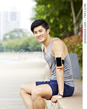 young asian jogger taking a break in city park, looking at camera with a big smile young asian jogger taking a break in city park, looking at camera with a big smile 79411246