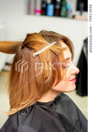 The female client receiving a haircut at the beauty salon, young woman enjoying getting a new hairstyle. The female client receiving a haircut at the beauty salon, young woman enjoying getting a new hairstyle. 79413648