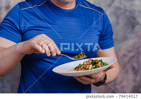 Salad with cucumber, tomato and green onions on a plate. A man holding a plate of salad Salad with cucumber, tomato and green onions on a plate. A man holding a plate of salad 79414017
