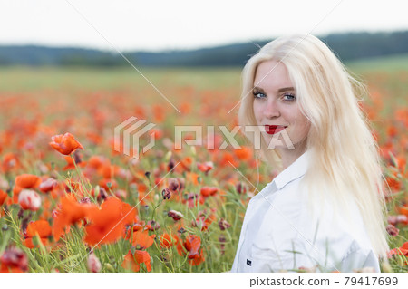 Portrait of blonde young woman posing in red poppy field. 79417699
