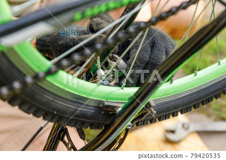 Bike mechanic man repairs bicycle in bicycle repair shop, outdoor. Hand of cyclist bicyclist examines, fixes modern cycle transmission system. Bike maintenance, sport shop concept. Bike mechanic man repairs bicycle in bicycle repair shop, outdoor. Hand of cyclist bicyclist examines, fixes modern cycle transmission system. Bike maintenance, sport shop concept. 79420535