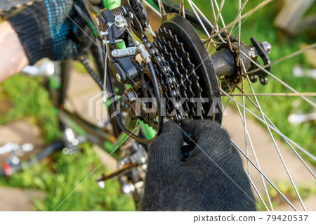 Bike mechanic man repairs bicycle in bicycle repair shop, outdoor. Hand of cyclist bicyclist examines, fixes modern cycle transmission system. Bike maintenance, sport shop concept. 79420537