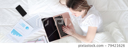 Woman lying in bed with laptop and documents top view Woman lying in bed with laptop and documents top view 79421626