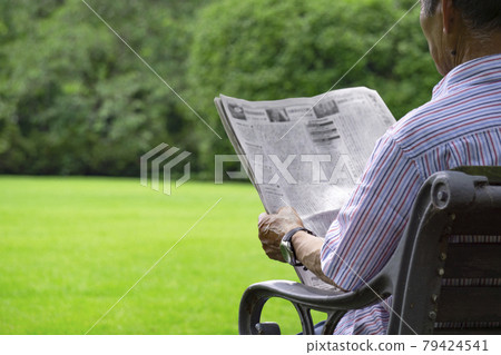 Elderly or middle-aged reading a newspaper on a park bench Elderly or middle-aged reading a newspaper on a park bench 79424541