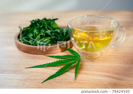 A glass of hot marijuana tea on the wooden table. Cannabis herbal tea with dried leaves 79424595