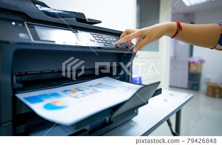 Office worker prints paper on multifunction laser printer. Copy, print, scan, and fax machine in office. Document and paper work. Print technology. Hand press on photocopy machine. Scanner equipment. 79426848