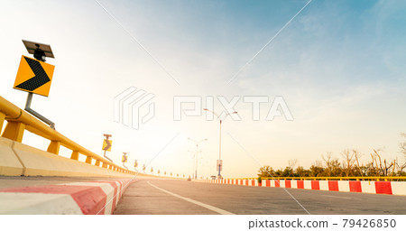 Curve concrete road with curve traffic sign beside the sea at sunset time. Solar panel energy on yellow curve traffic sign. Road trip on summer vacation. Blur car driving. Summer travel by car. 79426850