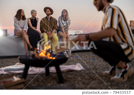 Friends by a fireplace on the rooftop at sunset 79433557