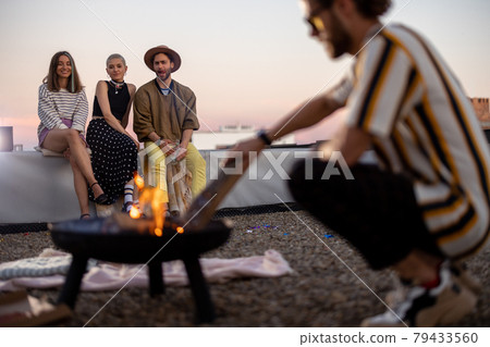 Friends by a fireplace on the rooftop at sunset 79433560