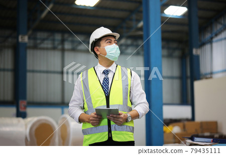 Warehouse worker man with safety hard hat is checking order details with a digital tablet at inventory room 79435111