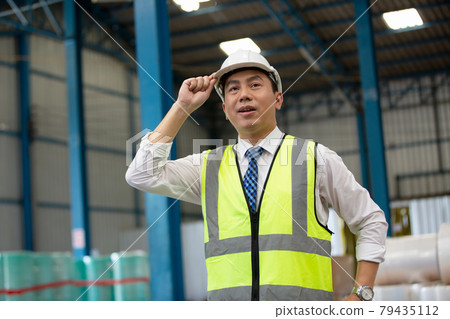 Warehouse worker man with safety hard hat is checking order details with a digital tablet at inventory room 79435112