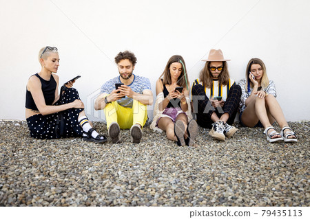 Friends sitting in a row with smartphones 79435113