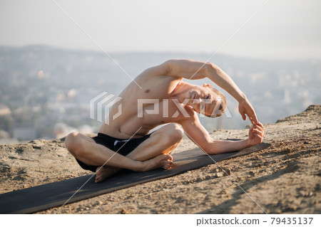 Sportsman doing flexible exercises on yoga mat outdoors Sportsman doing flexible exercises on yoga mat outdoors 79435137
