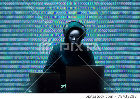 Anonymous hacker wearing face mask working on computer in dark room 79438288
