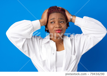 Young afro woman holding her head against blue background 79438290