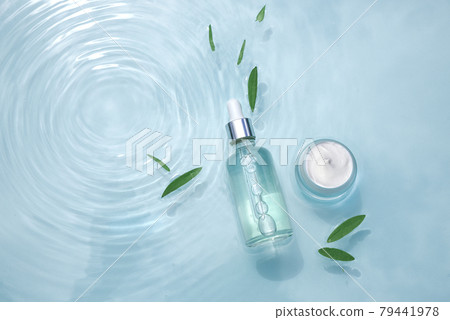 Set of moisturizing cosmetic products on water with drops. Glass bottle with pipette, serum, collagen and jar of cream on aqua surface with waves Set of moisturizing cosmetic products on water with drops. Glass bottle with pipette, serum, collagen and jar of cream on aqua surface with waves 79441978